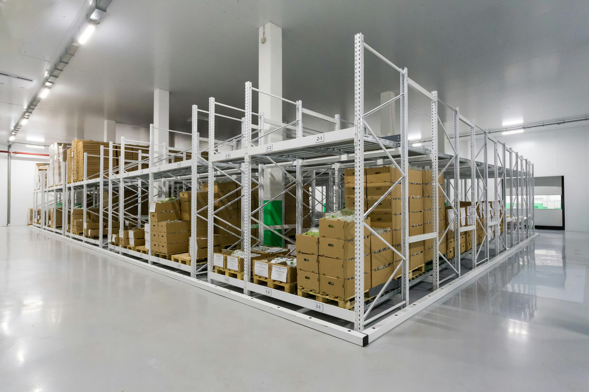 Blick in eine helle, weiß ausgekleidete Lagerhalle in der in einem Block-Design einige Regal mit Paketen stehen. Wir zeigen dir, was sich hinter einem Konsignationslager verbirgt und was du bei der Implementierung beachte solltest!