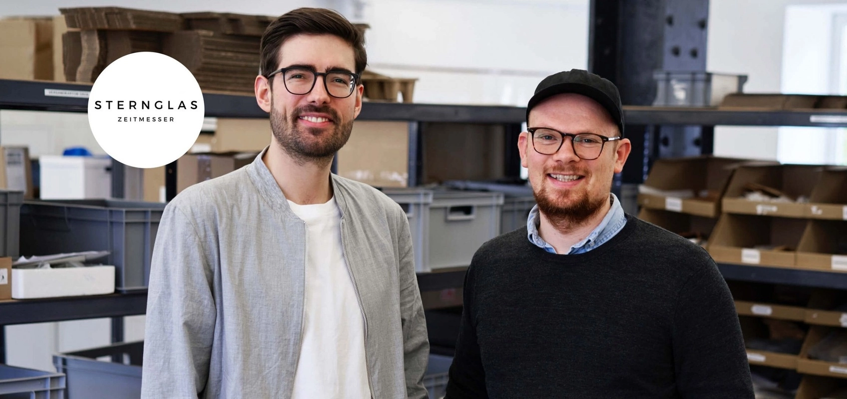 Henning und Dustin, Gründer von Sternglas, im Sternglas-Lager, mit Firmenlogo.