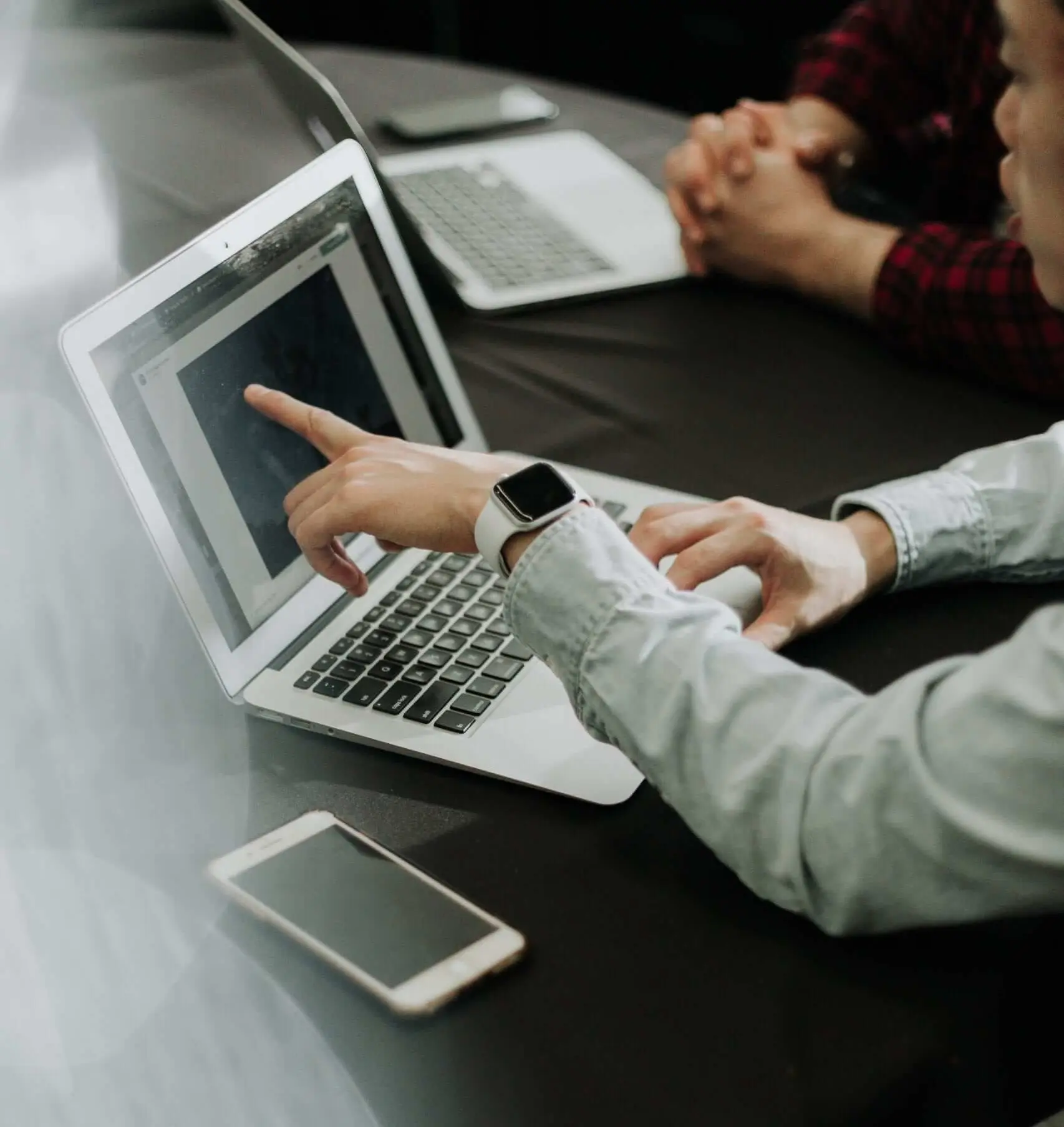 Blick auf einen Schreibtisch auf dem zwei aufgeklappte Laptops stehen. Zwei Personen sitzen nebeneinander und diskutieren. Wir zeigen dir, was sich hinter Multichannel Vertrieb verbirgt!