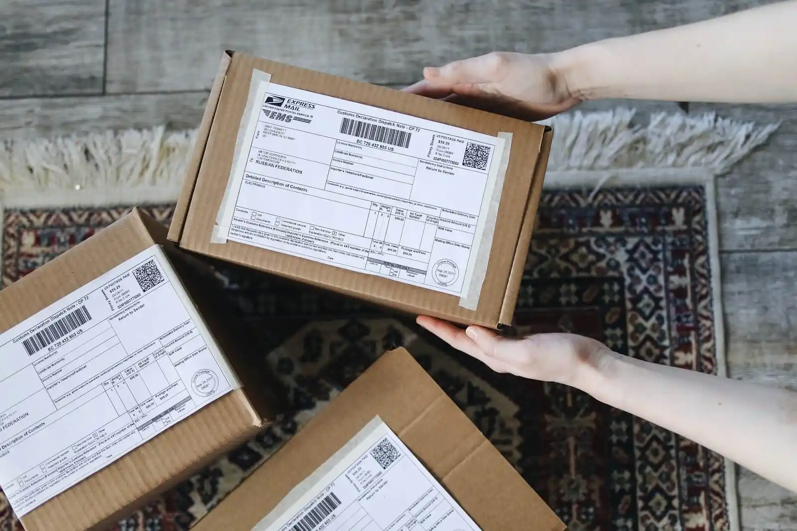 3 Kartons mit Etiketten und Hände halten einen Karton für Retoure.