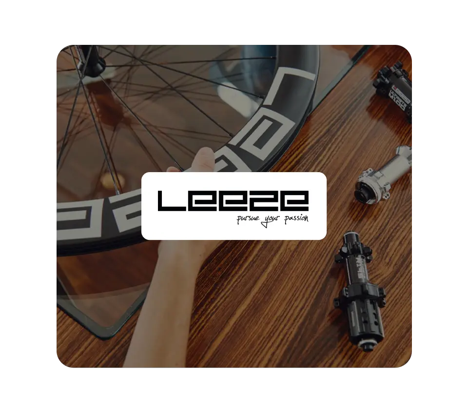 The "Leeze - pursue your passion" brand logo in a white box, overlaid on a background showing a bicycle wheel rim and various high-quality bike hubs on a polished wooden table.Xentral ERP for bike retail: 