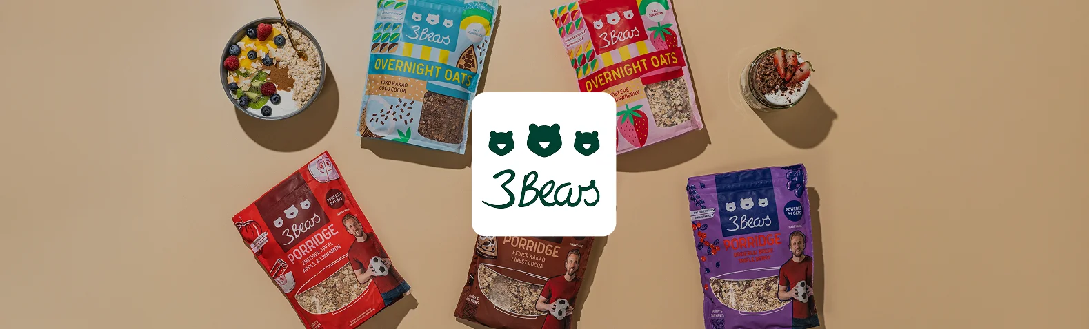 Produktübersicht von 3Bears: fünf bunte Beutel Porridge und Overnight Oats in Sorten wie Zimtiger Apfel, Feiner Kakao, Dreierlei Beere und Erdbeere, dazu angerichtete Porridge-Schale und Overnight-Oats-Glas mit Obst. Das 3Bears-Logo mit drei Bärenköpfen steht in der Mitte.