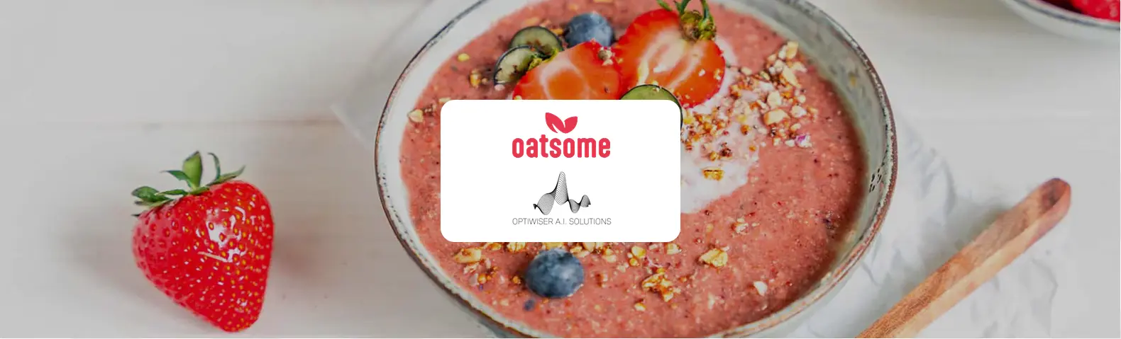 Schale mit rosa Erdbeer-Porridge, garniert mit frischen Erdbeeren, Heidelbeeren, Nüssen und Joghurt, daneben ein Holzlöffel. In der Bildmitte die Logos von Oatsome und Optiwiser A.I. Solutions.