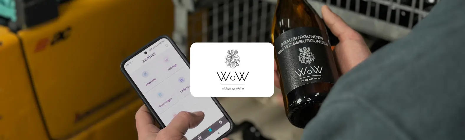 Person im Lager hält in einer Hand ein Smartphone mit der Xentral-App (Angebote, Aufträge, Lieferscheine, Rechnungen) und in der anderen eine Flasche Grauburgunder und Weißburgunder von Wolfgangs Weine. In der Bildmitte das WoW-Logo mit Wappen.