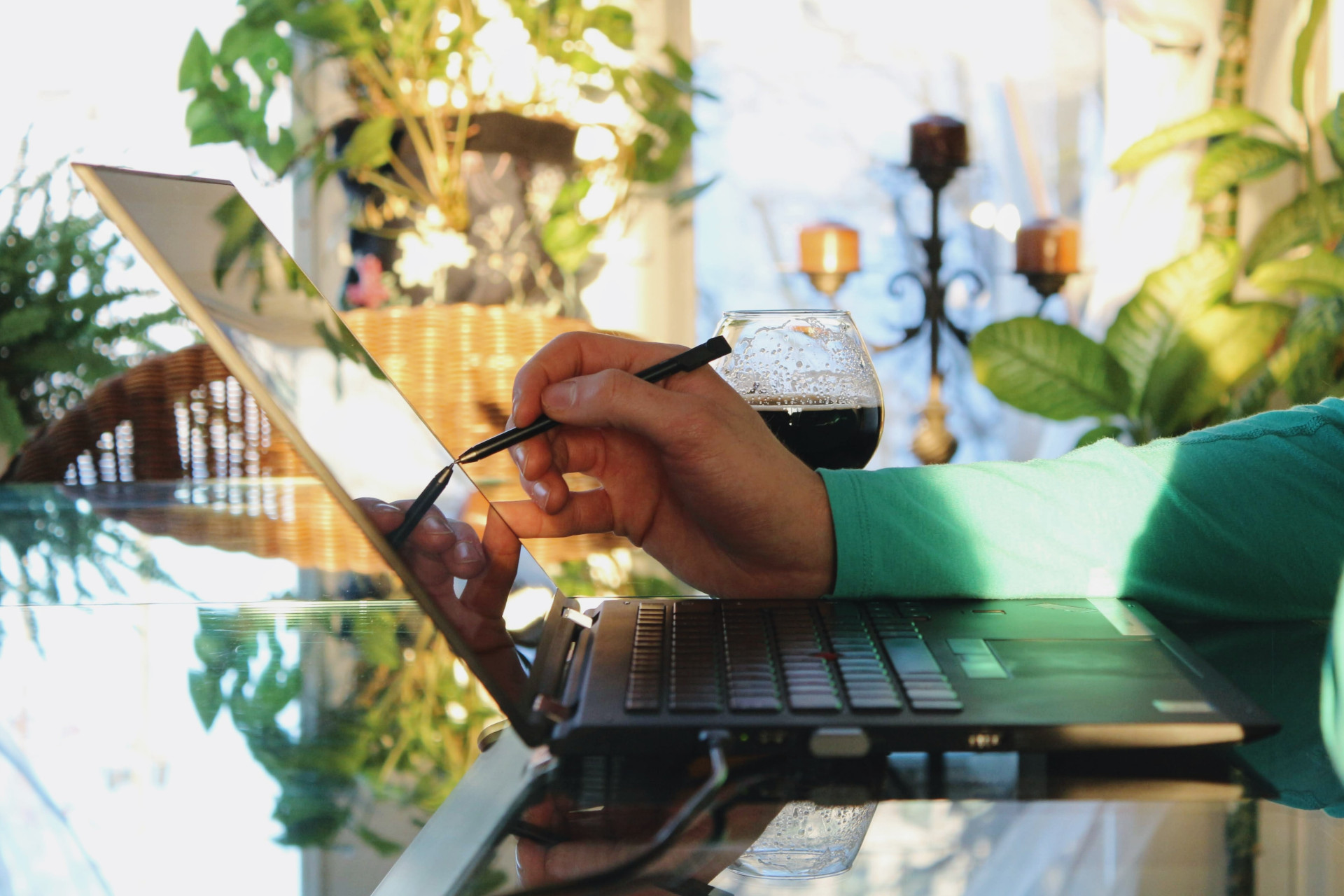 Blick von der Seite auf einen aufgeklappten Laptop auf einem Glastisch vor dem eine Person sitzt. Im Hintergrund sind unscharf Zimmerpflanzen und ein Glas mit einer dunklen Flüssigkeit zu erkennen. Dank Cloud-ERP kannst du von überall auf deine Daten zugreifen. Wir zeigen dir, was sich dahinter verbirgt!