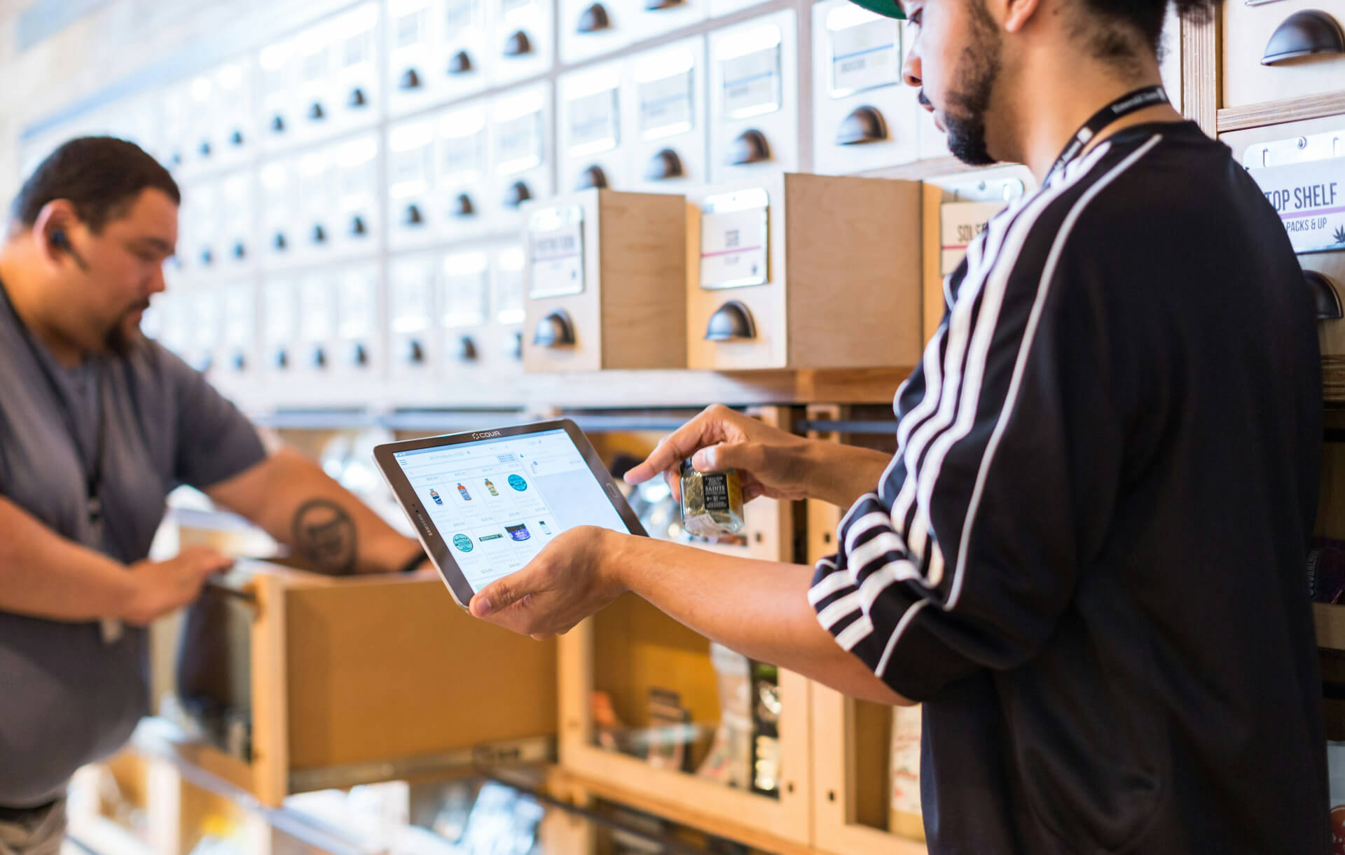 Blick in einen Laden mit einer großen Apothekerwand. Eine Person sucht etwas in einem Schieber. Die andere Person tippt auf einem iPad. Wir zeigen dir, was sicher hinter der permanenten Inventur verbirgt!